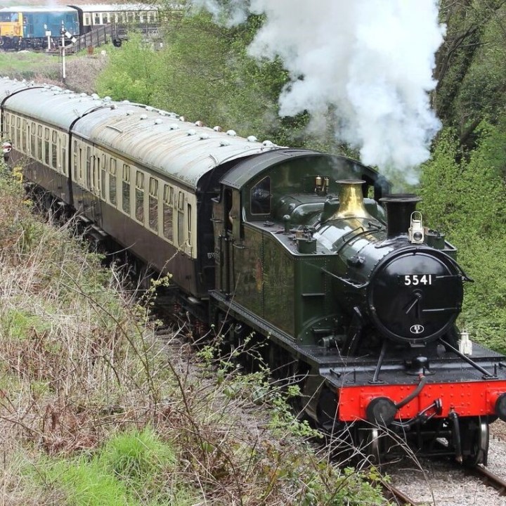 a steam engine train traveling down train tracks near a forest