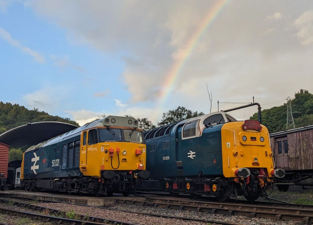 Two vintage trains on tracks with a rainbow in the sky.
