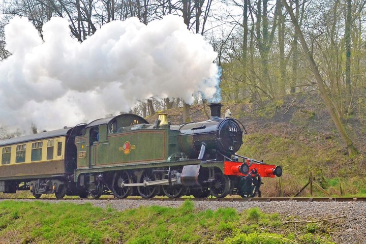 a steam engine train traveling down train tracks near a forest