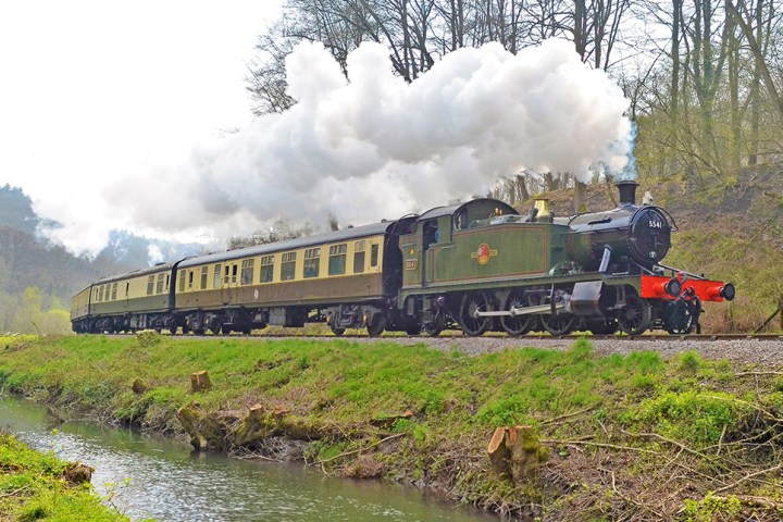 a steam engine train traveling down train tracks near a forest