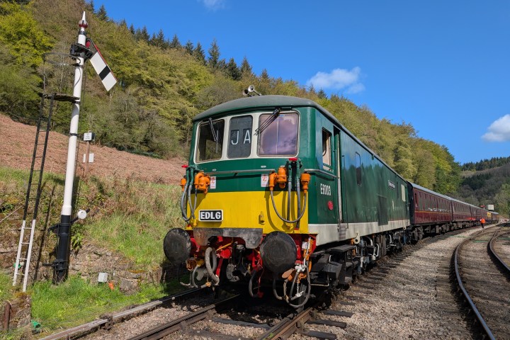 Vintage green train on tracks with semaphore signal, under blue sky.