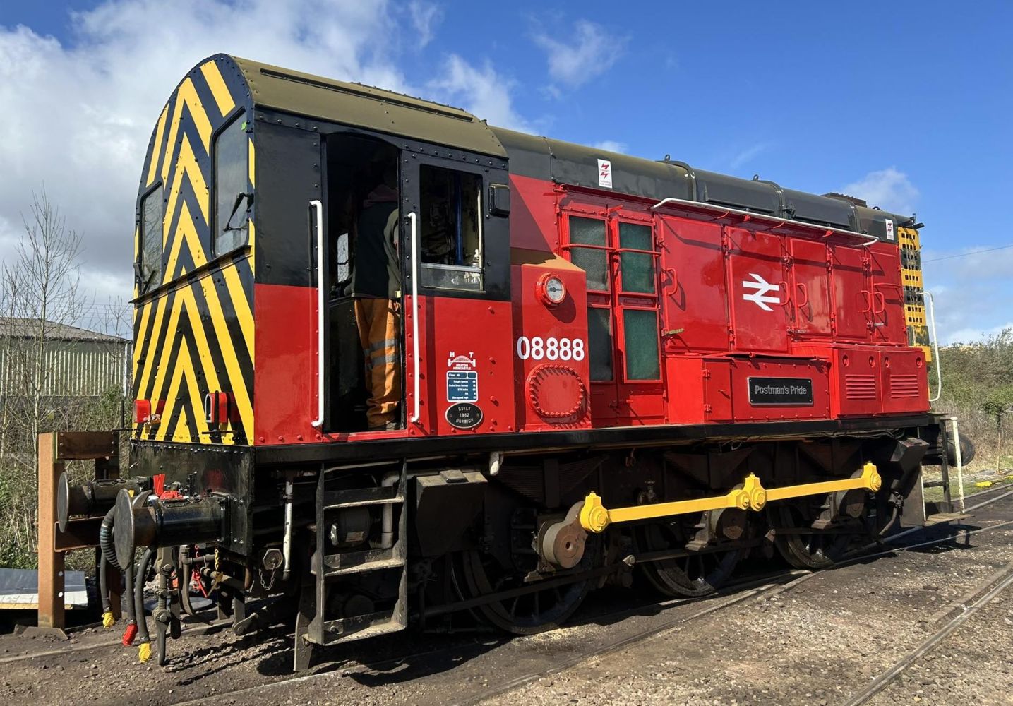 Red and black train engine with striped rear, labeled 'Postman's Pride' on tracks.