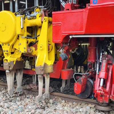 Close-up of a red and yellow railway maintenance machine on train tracks.