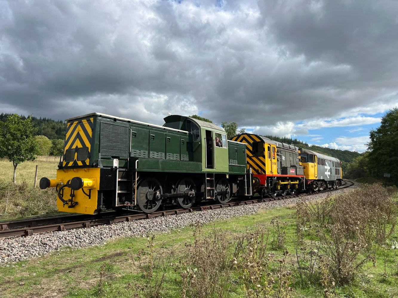 Three vintage trains on tracks in a countryside setting with cloudy sky.